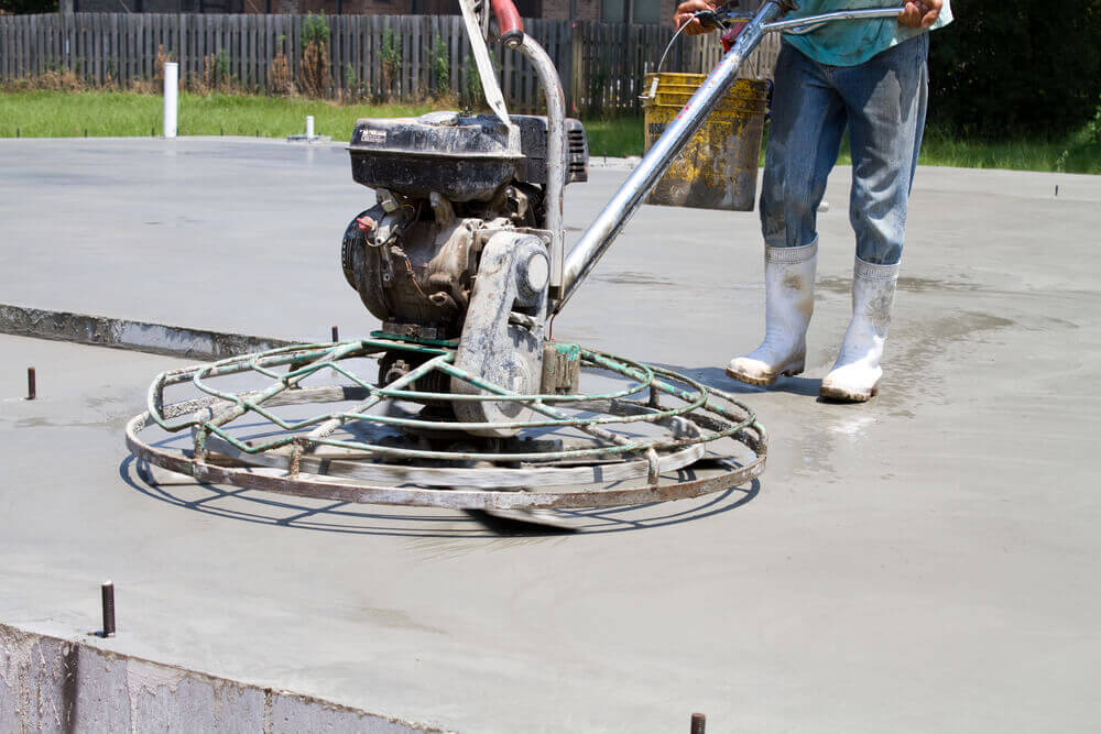 concrete worker with a motorized trowel machine on a freshly poured concrete slab