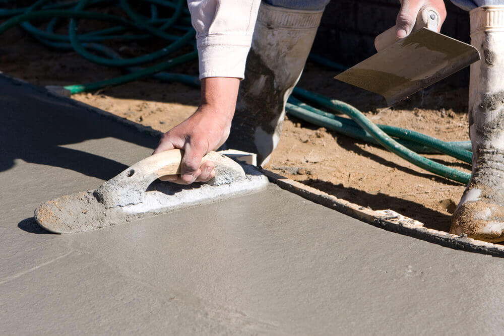 Close up of a concrete worker using a trowel to level off the side of some concrete driveways