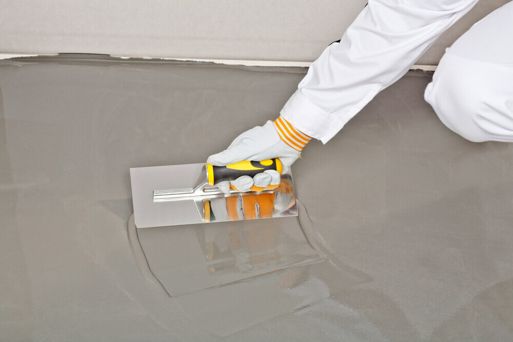 A concrete resurfacing worker with a trowel spreading around a resurfacing liquid in a white jump suit